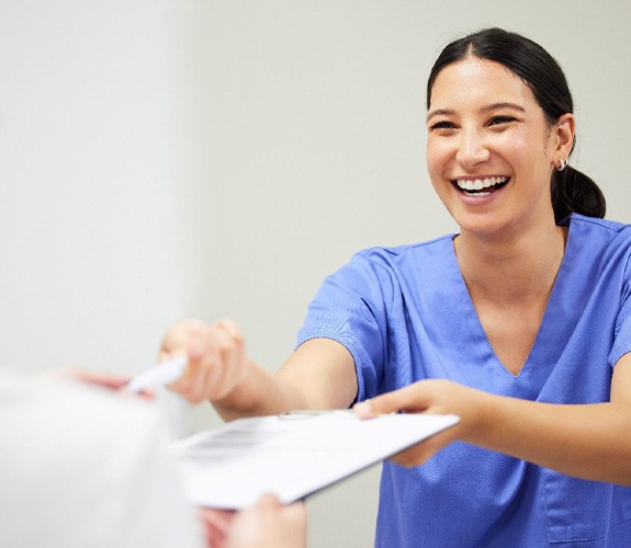 Dental assistant smiling while handing patient form